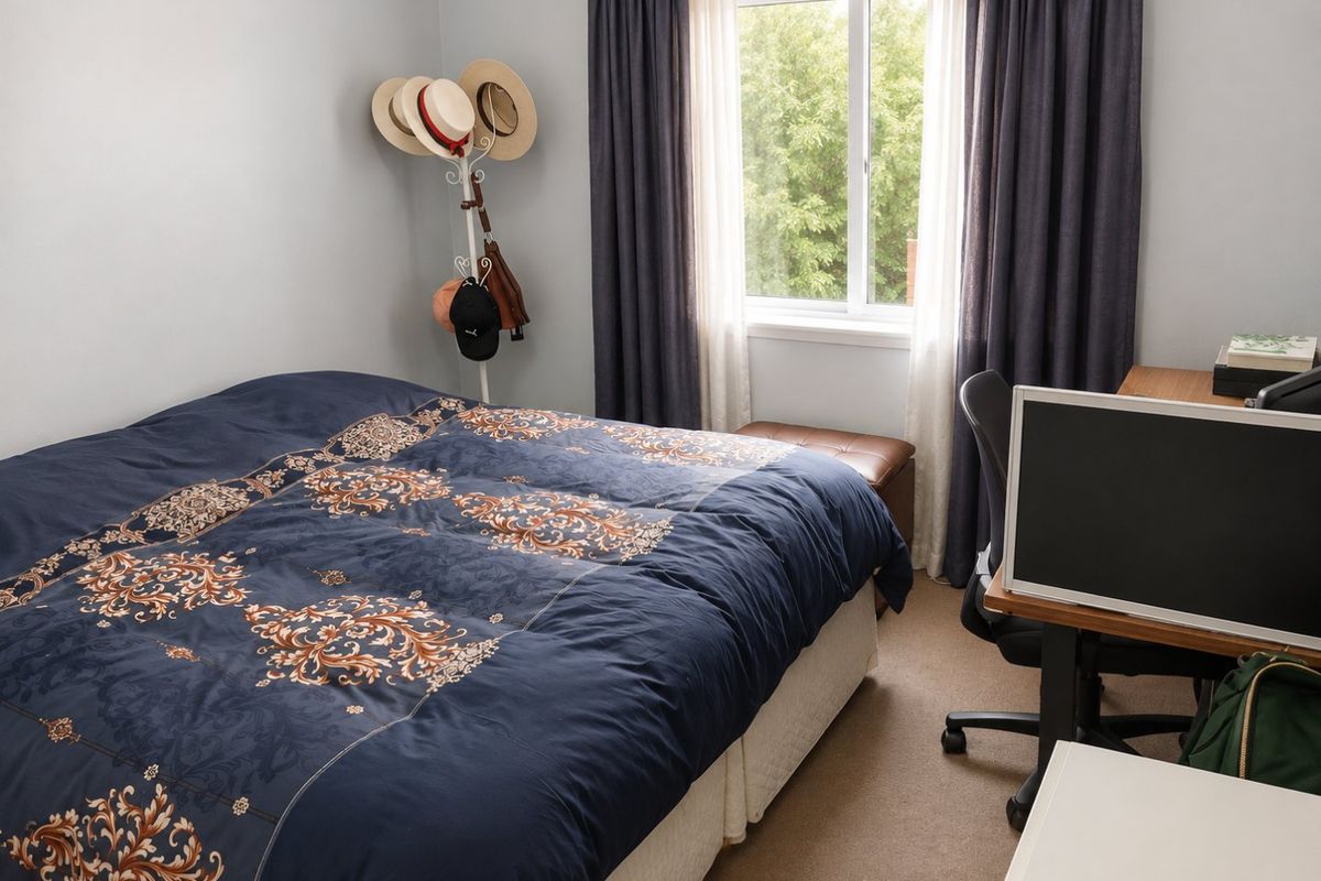 A functional bedroom featuring carpeted flooring and a window with curtains, providing natural light and a comfortable living space.