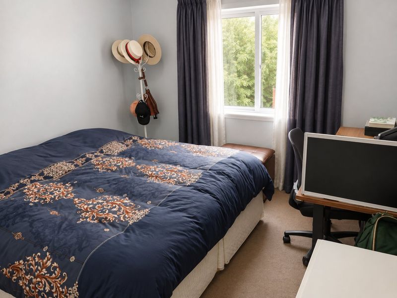 A functional bedroom featuring carpeted flooring and a window with curtains, providing natural light and a comfortable living space.