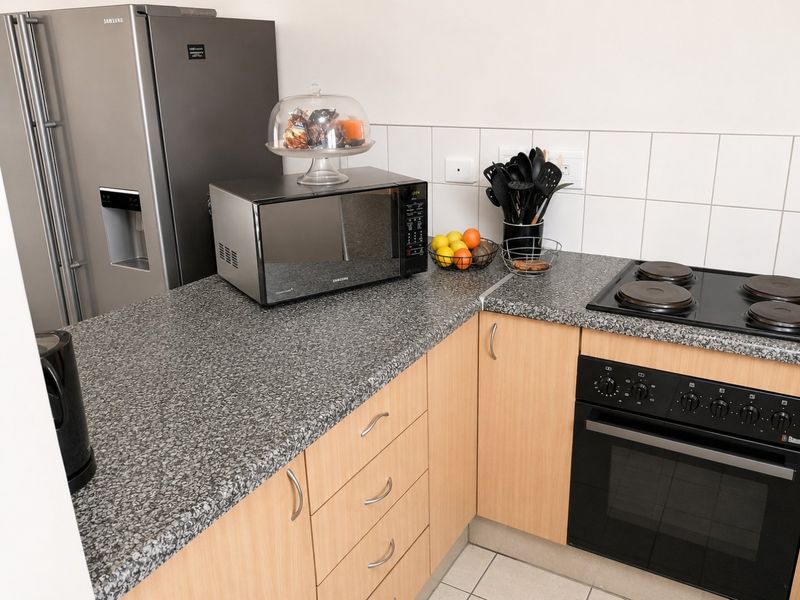 A functional kitchen featuring laminate countertops, light wood cabinetry, a built-in oven with an electric hob, and a tiled backsplash.