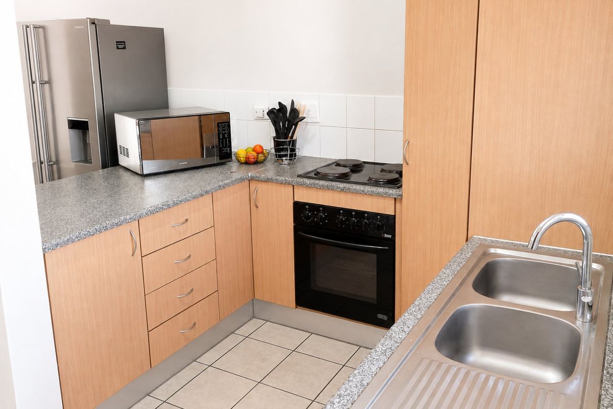 A functional kitchen featuring light wood-finish cabinetry, granite-look laminate countertops, a built-in oven with electric hob, and a double stainless steel sink.