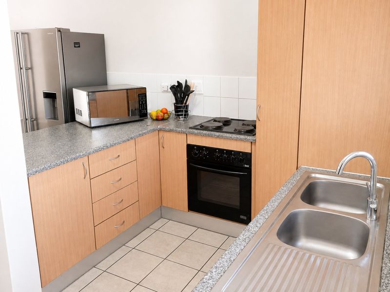 A functional kitchen featuring light wood-finish cabinetry, granite-look laminate countertops, a built-in oven with electric hob, and a double stainless steel sink.