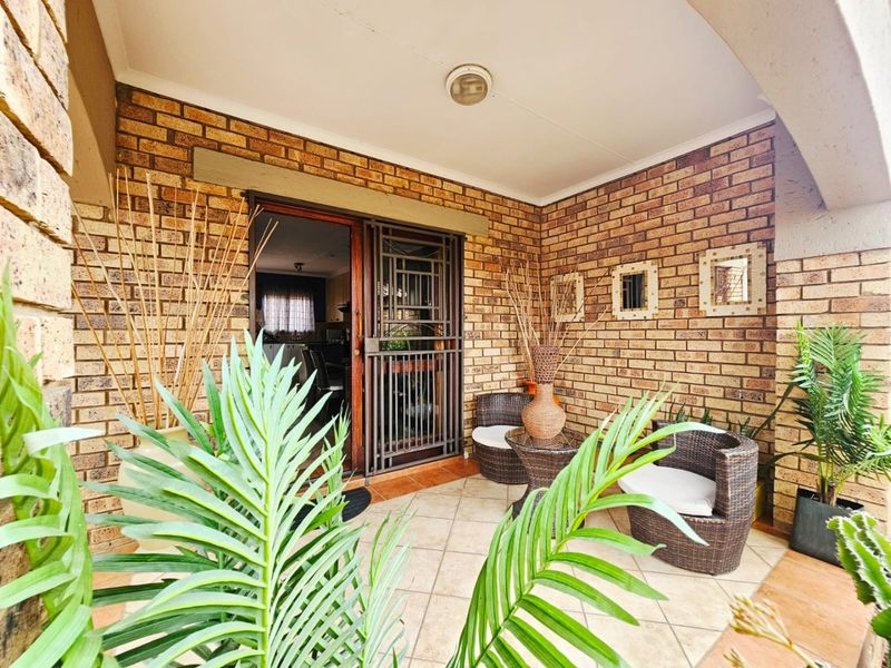 A covered patio area featuring exposed brick walls, tiled flooring, and a secure metal entrance gate leading into the home.