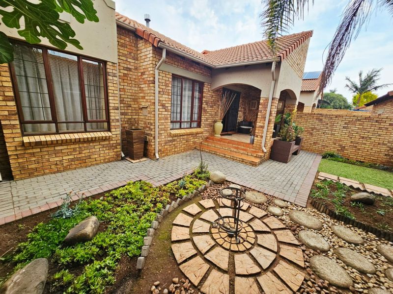 A well-maintained townhouse rear exterior featuring a face brick facade, covered entrance, paved patio area, and a landscaped garden with stone pathways.