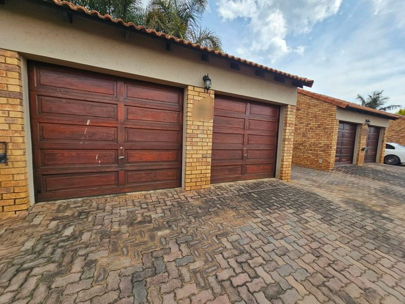Exterior view of a townhouse complex featuring multiple garages with wooden doors and a paved driveway.