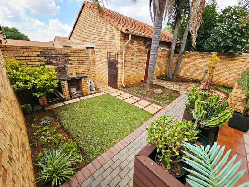 Private rear courtyard featuring a built-in brick braai, paved pathways, and established garden beds enclosed by high brick boundary walls.