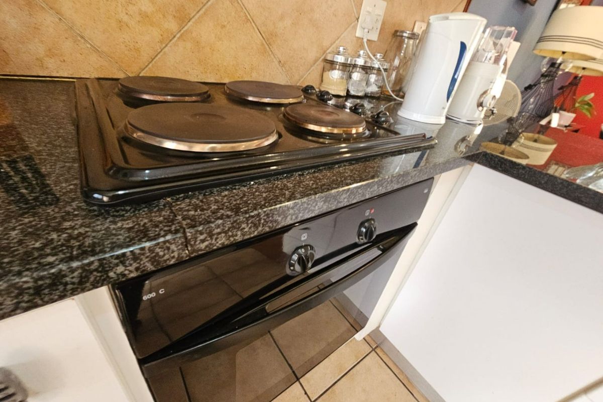 A kitchen area featuring a built-in electric oven, hob, granite countertops, and tiled backsplash.