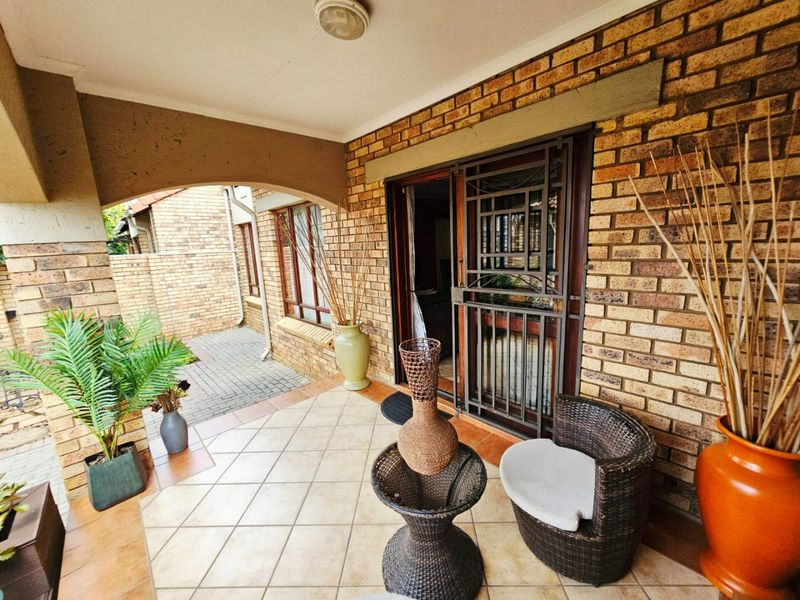 A covered patio area featuring brick walls, tiled flooring, and a secure metal gate entrance, providing a functional outdoor space.