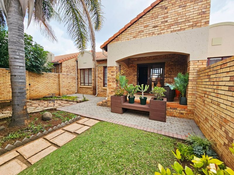 A well-maintained rear exterior view of a face brick townhouse featuring a covered patio, paved walkway, and a private garden area.
