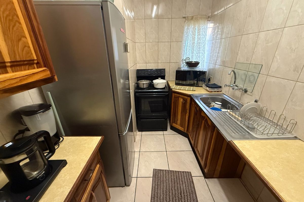 A compact kitchen featuring wooden cabinetry, laminate countertops, tiled wall finishes, and a freestanding oven, offering a functional layout for daily meal preparation.