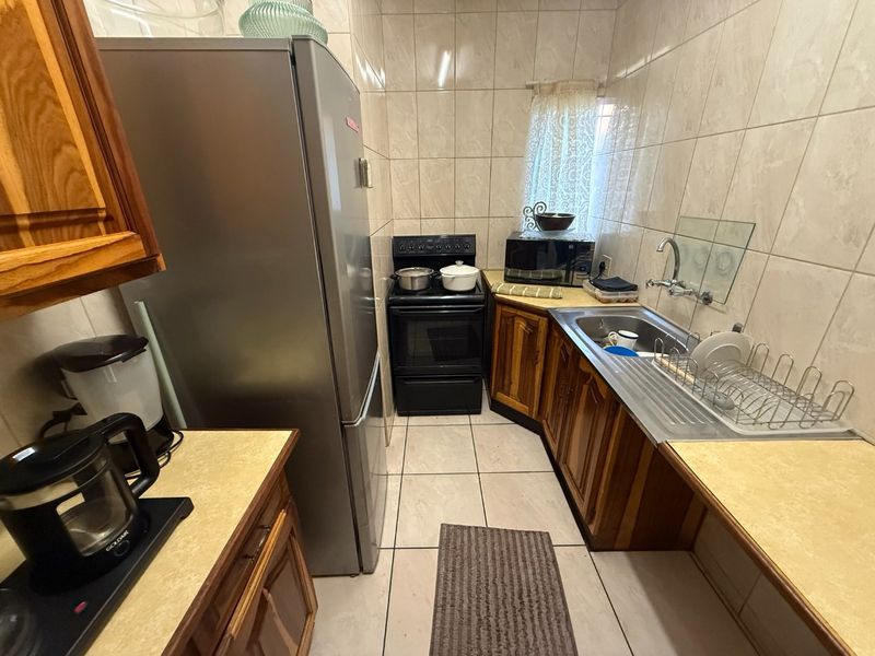 A compact kitchen featuring wooden cabinetry, laminate countertops, tiled wall finishes, and a freestanding oven, offering a functional layout for daily meal preparation.