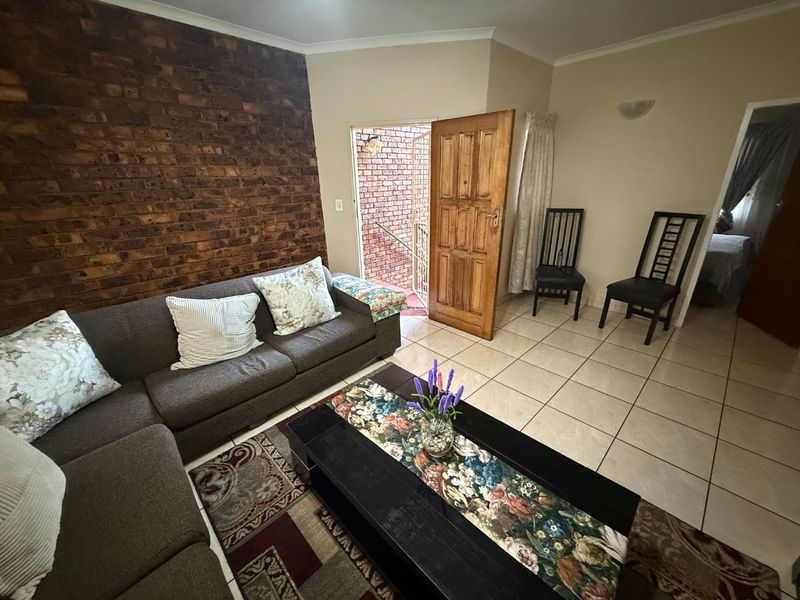 Living room featuring an exposed brick accent wall, ceramic tiled flooring, and direct access to an exterior area through a timber door.