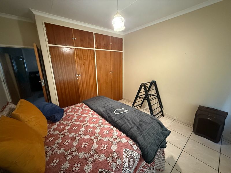 A bedroom featuring tiled flooring and built-in wooden cupboards, offering a functional space with neutral wall finishes.