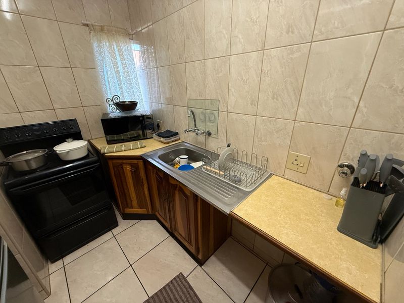 Compact kitchen featuring tiled walls and flooring, wooden cabinetry, a stainless steel sink, and a freestanding stove.