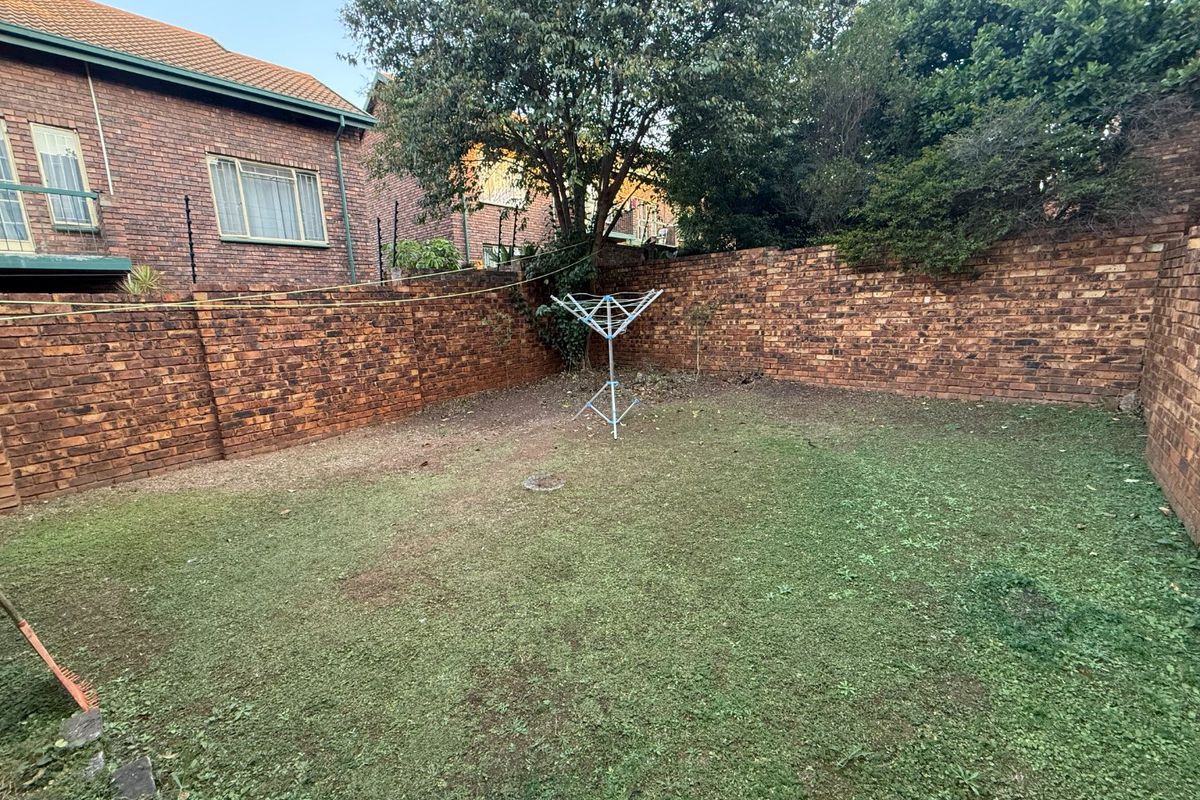 A private rear garden area enclosed by high brick boundary walls, featuring a lawn space and established trees.