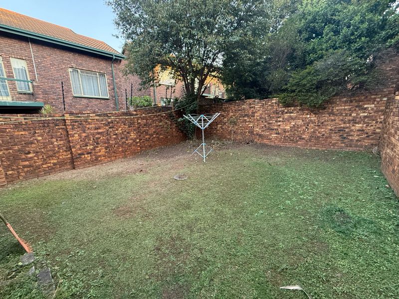 A private rear garden area enclosed by high brick boundary walls, featuring a lawn space and established trees.