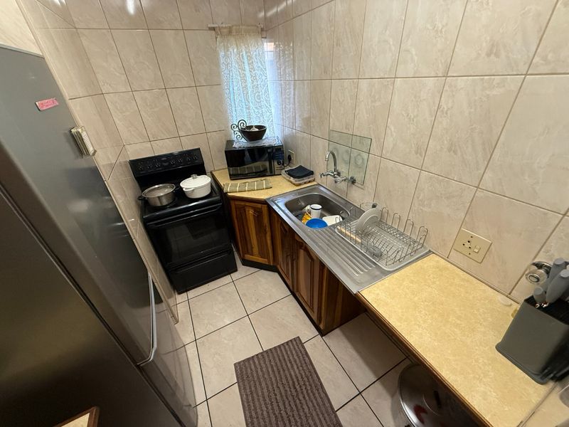 Compact kitchen featuring tiled walls, wooden cabinetry, laminate countertops, and a stainless steel sink with a freestanding stove.