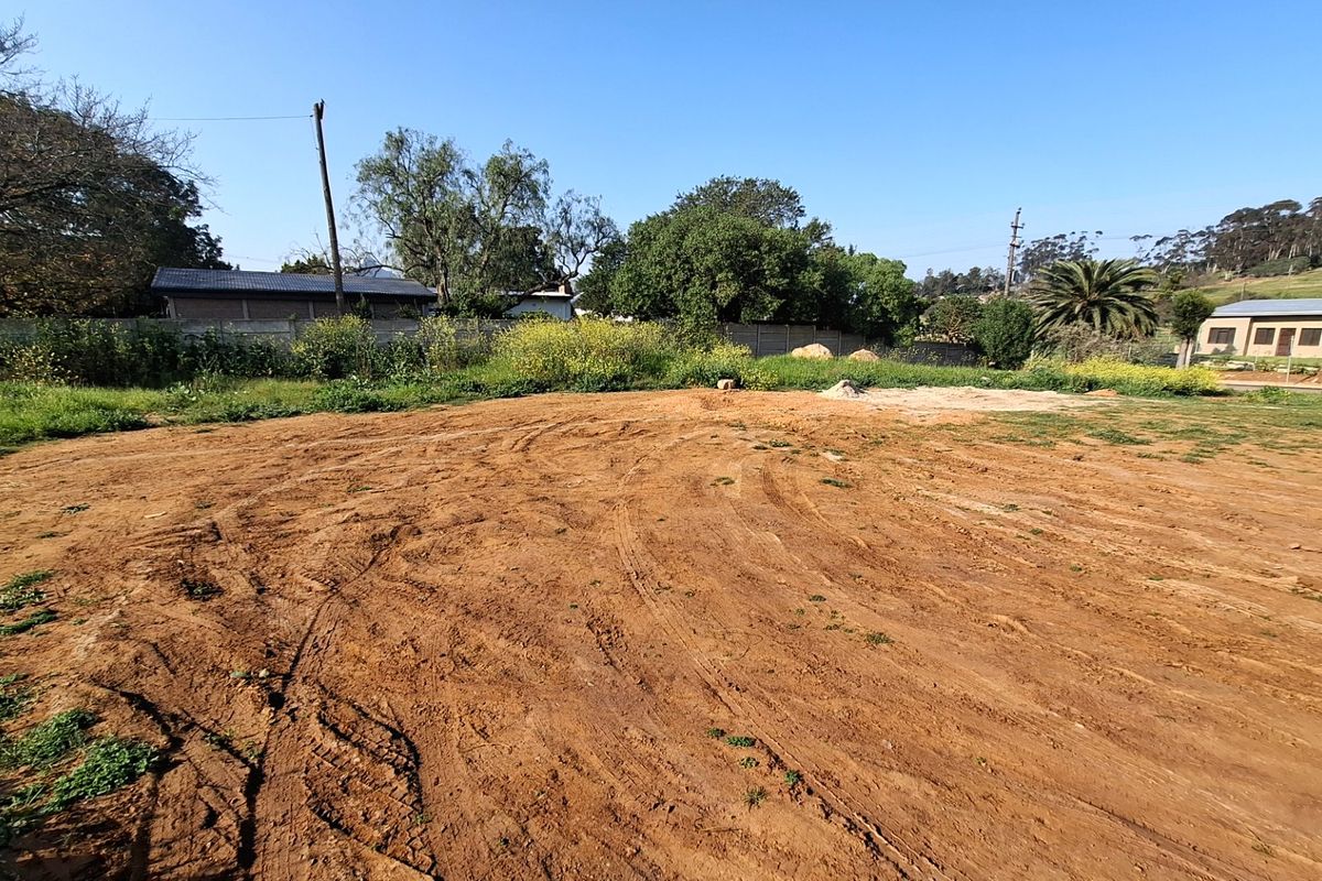 A vacant residential plot featuring cleared earth, perimeter fencing, and surrounding mature trees, offering a blank canvas for future development.