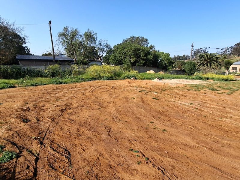 A vacant residential plot featuring cleared earth, perimeter fencing, and surrounding mature trees, offering a blank canvas for future development.