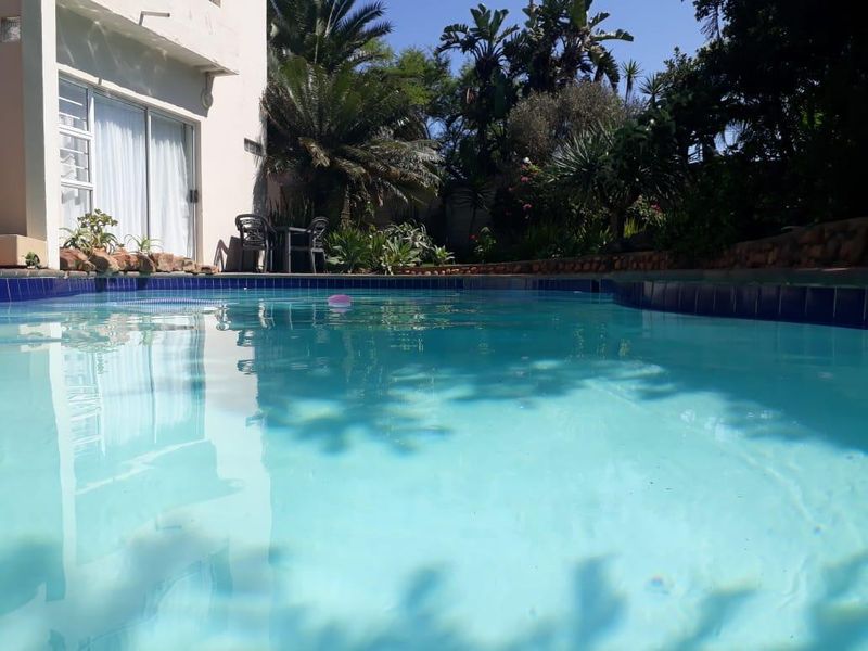 A private swimming pool area featuring tiled coping, adjacent to a landscaped garden and the building's exterior sliding glass doors.