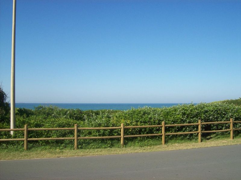 A scenic view of the ocean horizon featuring a timber post and rail fence bordering a paved road.