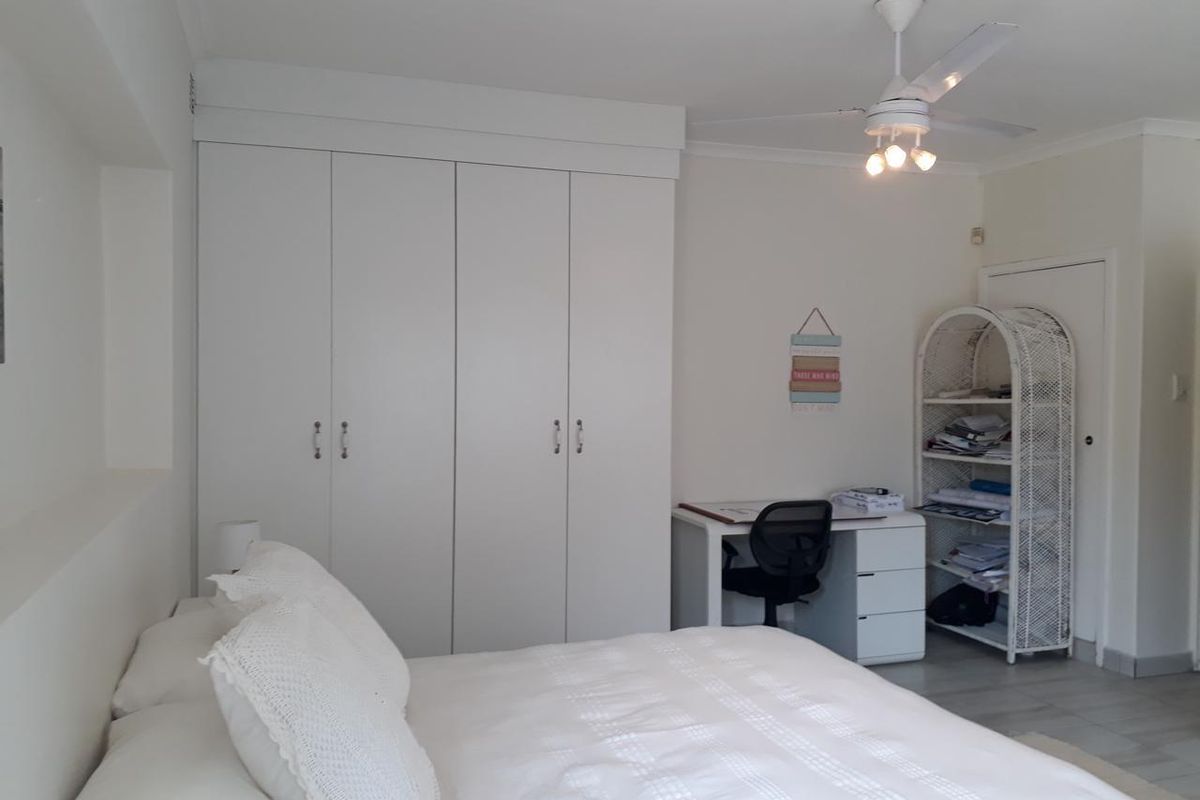 A bright bedroom featuring neutral walls, tiled flooring, a ceiling fan, and ample built-in cupboard storage.