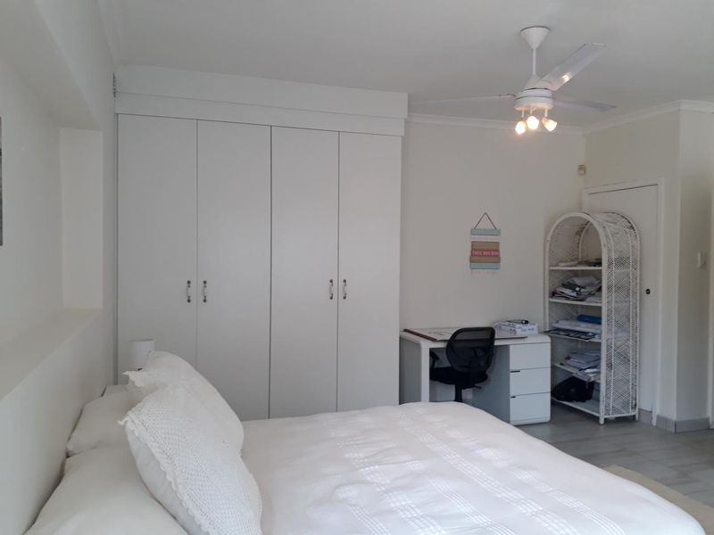 A bright bedroom featuring neutral walls, tiled flooring, a ceiling fan, and ample built-in cupboard storage.