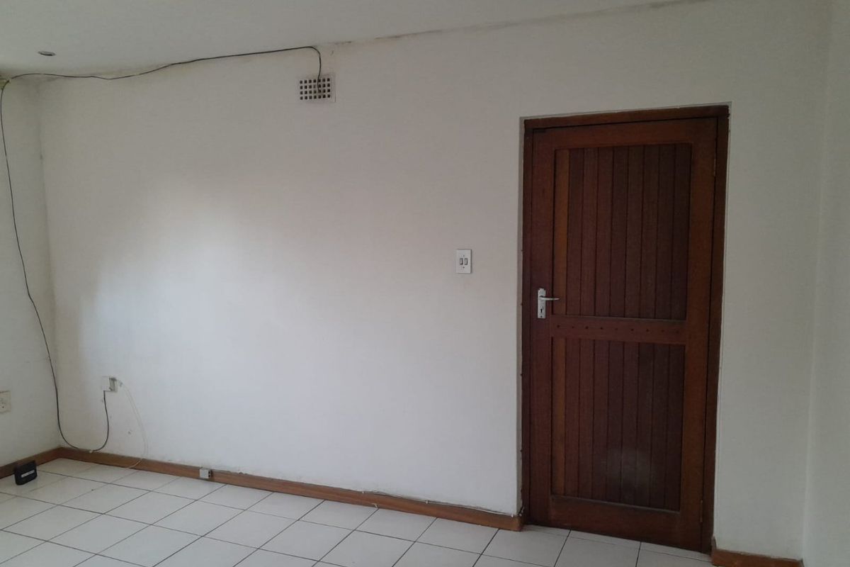 An empty living area featuring white walls, tiled flooring, and a solid timber door, requiring minor cosmetic updates and electrical cable management.