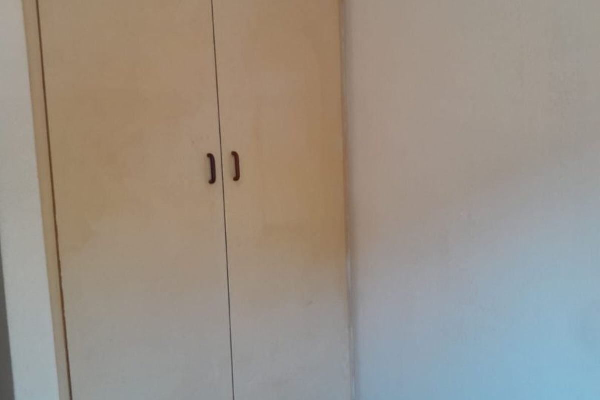 A simple bedroom corner featuring a built-in wardrobe with plain doors and neutral wall finishes.