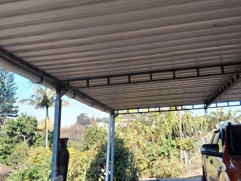 An open-sided carport structure with a corrugated metal roof, providing covered parking space on a concrete driveway.