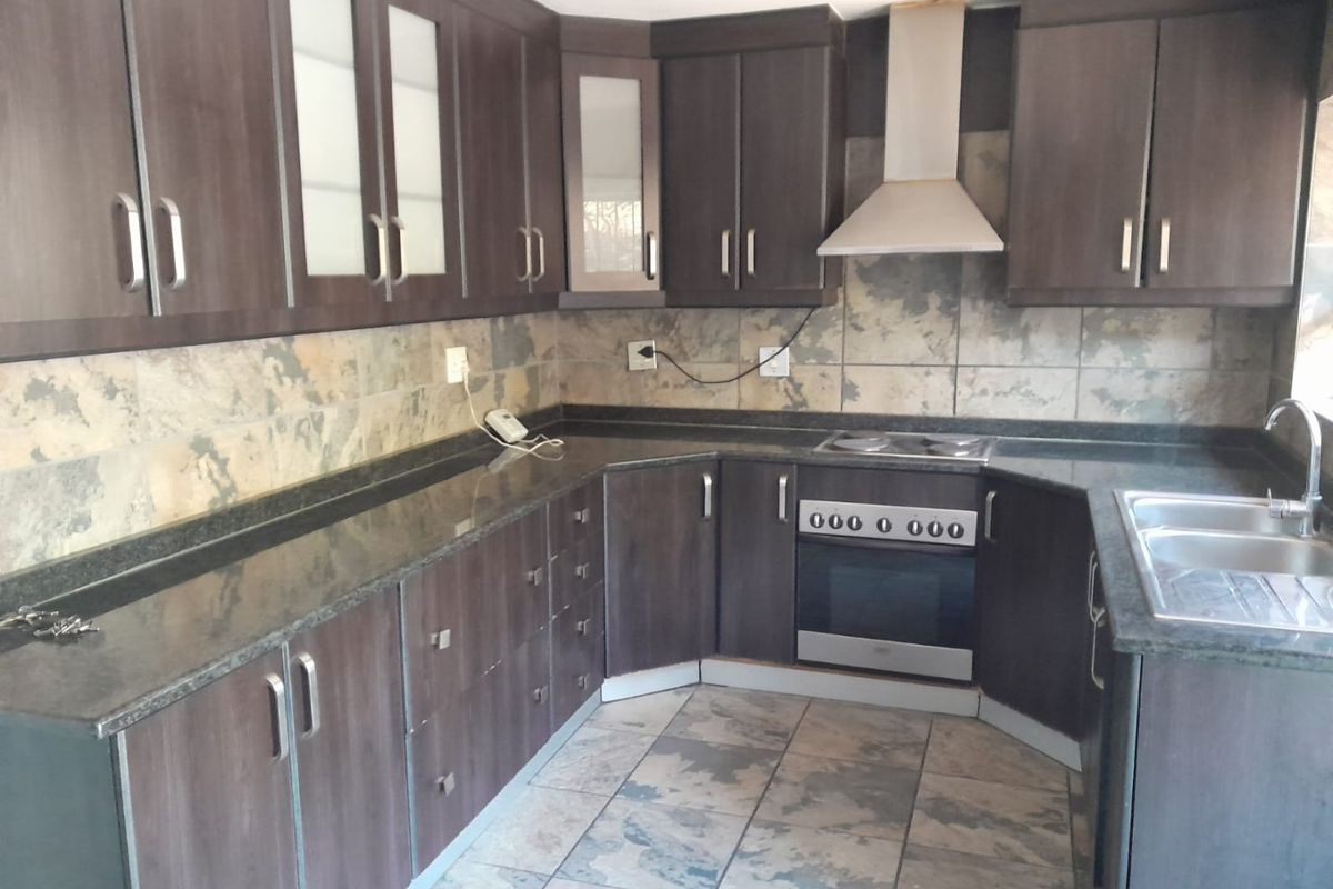 A functional kitchen featuring dark wood cabinetry, granite countertops, stone tile flooring, and built-in stainless steel appliances.