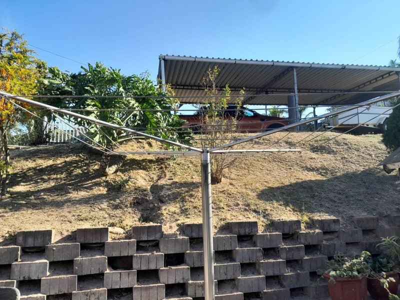 Rear garden area featuring a tiered concrete block retaining wall, a metal carport structure, and a rotary clothesline.