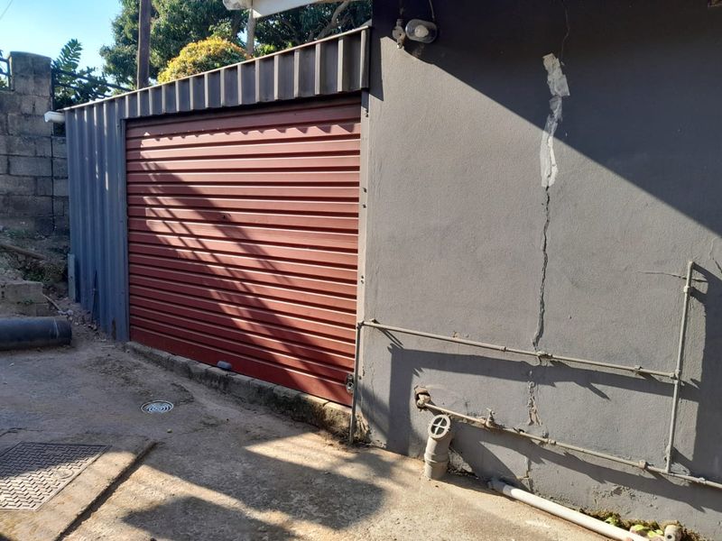 Exterior view of a garage featuring a red roller shutter door and visible structural cracking on the adjacent exterior wall.