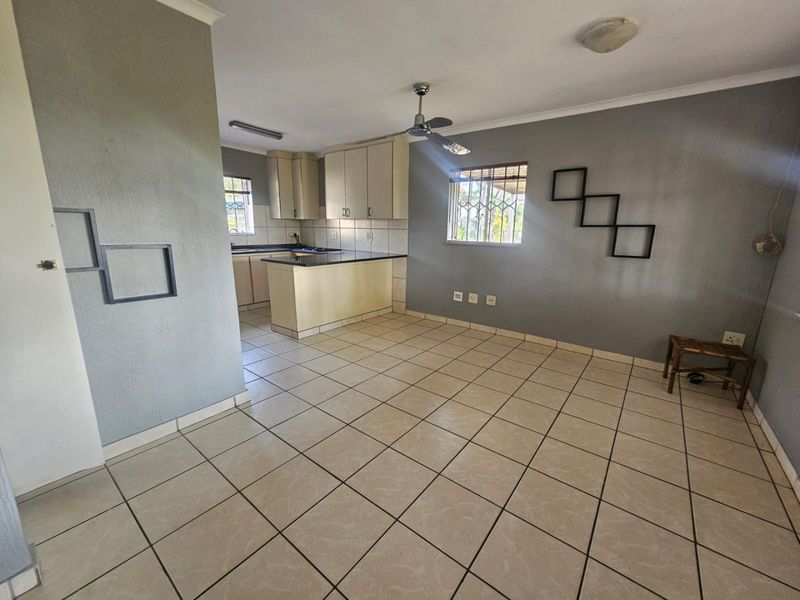 Open-plan living and kitchen area featuring tiled flooring, ceiling fan, and functional built-in cabinetry with laminate countertops.