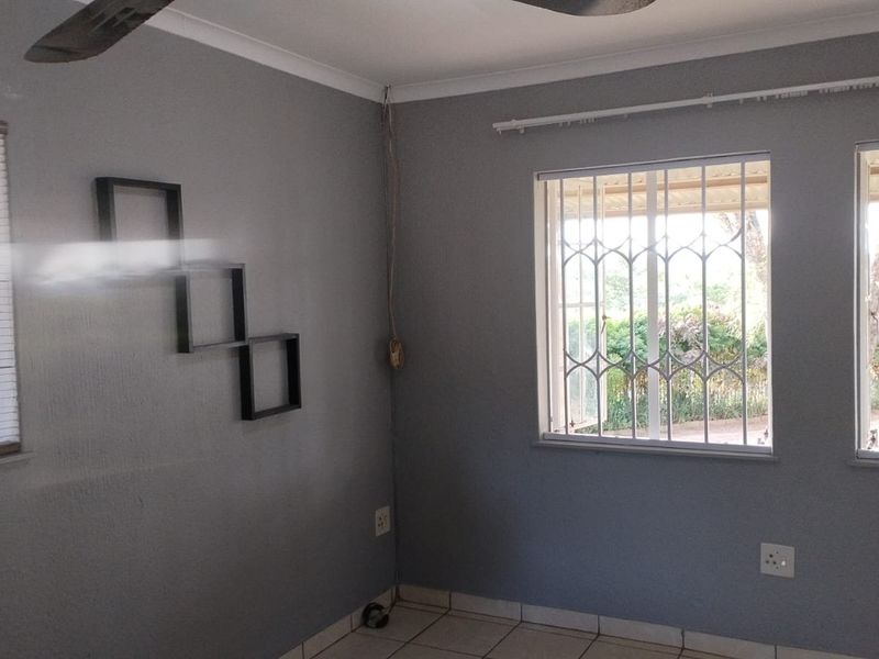 A bright, empty bedroom featuring tiled flooring, ceiling fan, and windows fitted with security bars.