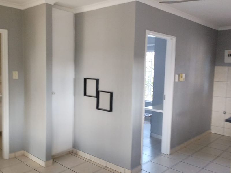 Open plan living area featuring tiled flooring, neutral grey walls, and access to an adjoining kitchen and bathroom space.
