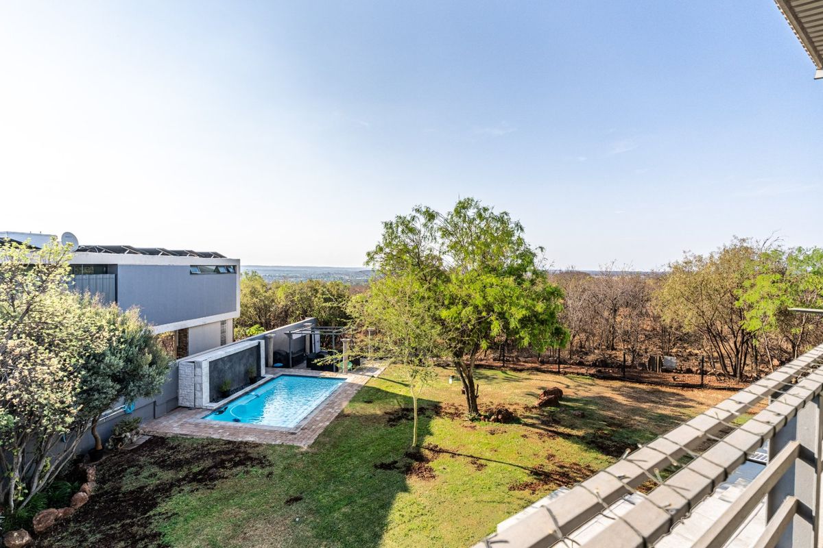 Rear view of the property featuring a swimming pool, landscaped garden, and solar panels on the roof, overlooking a natural bushveld landscape.