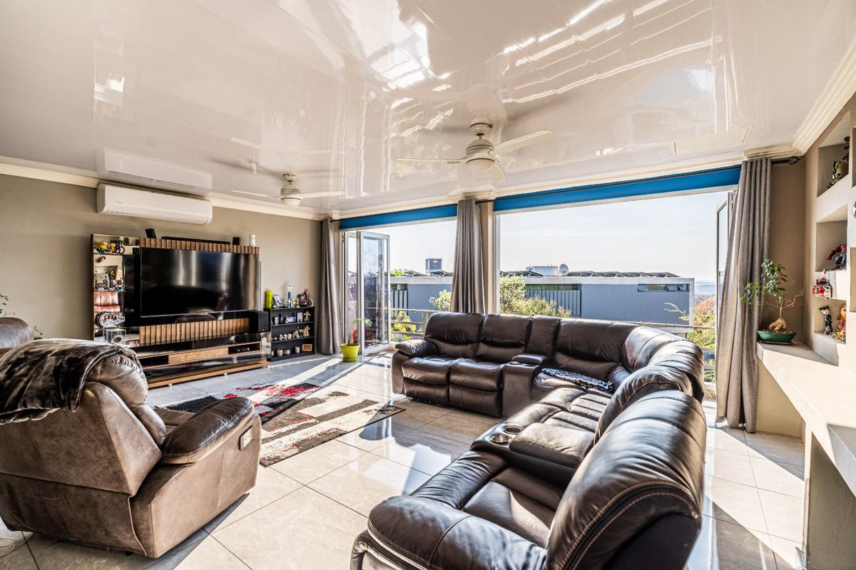 Spacious living room featuring a high-gloss ceiling, tiled floors, built-in media cabinetry, and large glass doors opening to an outdoor area with views.