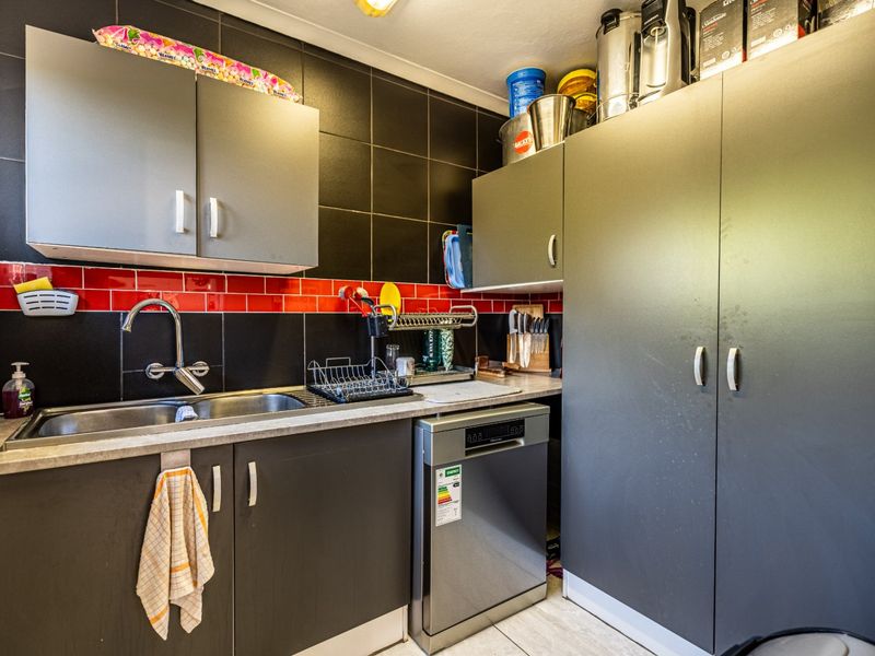 A functional scullery area featuring dark cabinetry, a stainless steel sink, and a contrasting red and black tiled splashback.