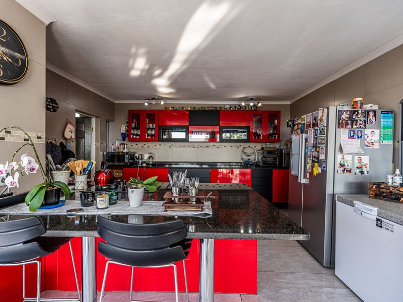 A functional kitchen featuring high-contrast red and black cabinetry, a large granite-topped island, and tiled flooring, offering ample workspace and storage.