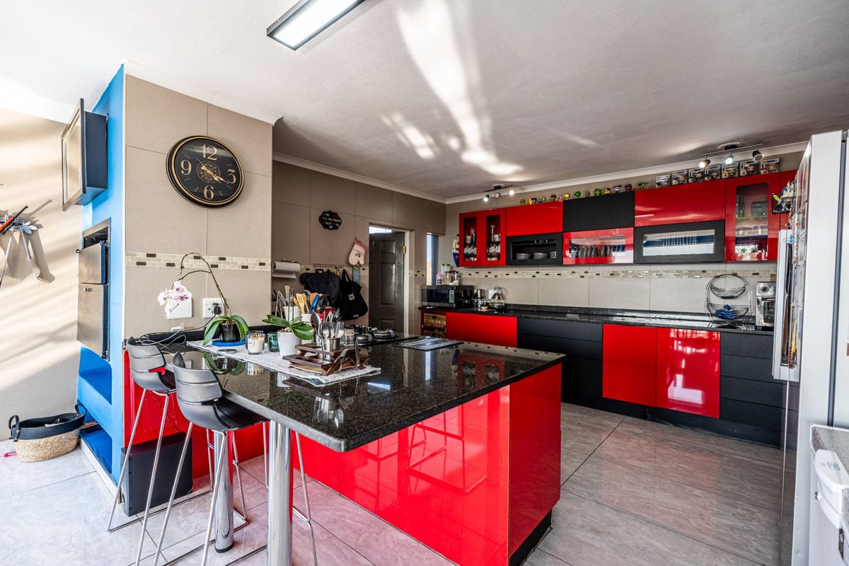 Modern kitchen featuring high-gloss red and black cabinetry, granite countertops, a breakfast bar, and tiled flooring with integrated appliances.