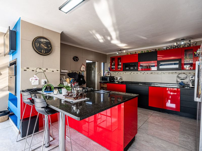 Modern kitchen featuring high-gloss red and black cabinetry, granite countertops, a breakfast bar, and tiled flooring with integrated appliances.