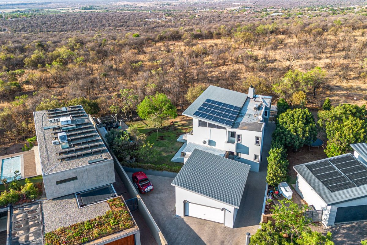 Aerial view of a modern residential property featuring multiple buildings, solar panel installations, paved driveway, and surrounding natural landscape.