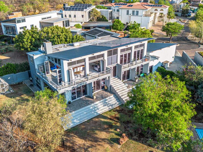 Aerial view of a modern multi-level residence featuring a metal roof with solar panels, expansive balconies, a paved patio, and a private swimming pool.