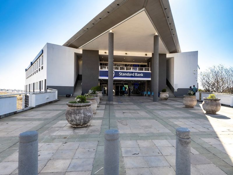 Modern commercial building entrance featuring a prominent triangular canopy, paved terrace area, and concrete structural columns.
