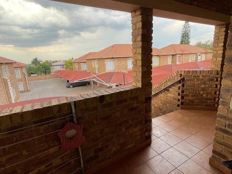 A covered balcony featuring exposed brickwork and tiled flooring, overlooking the apartment complex parking area.