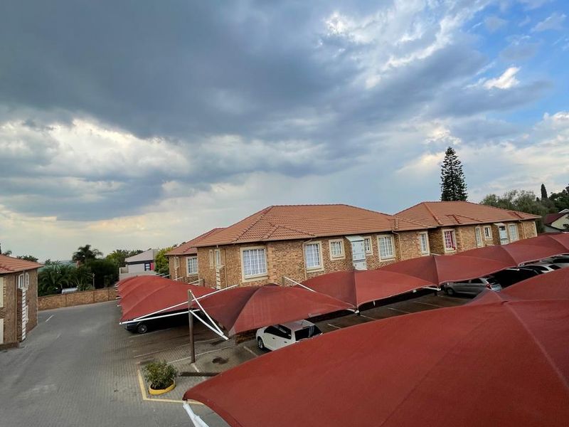 Exterior view of an apartment complex featuring brick facades, tiled roofing, and covered parking bays with shade cloth structures.