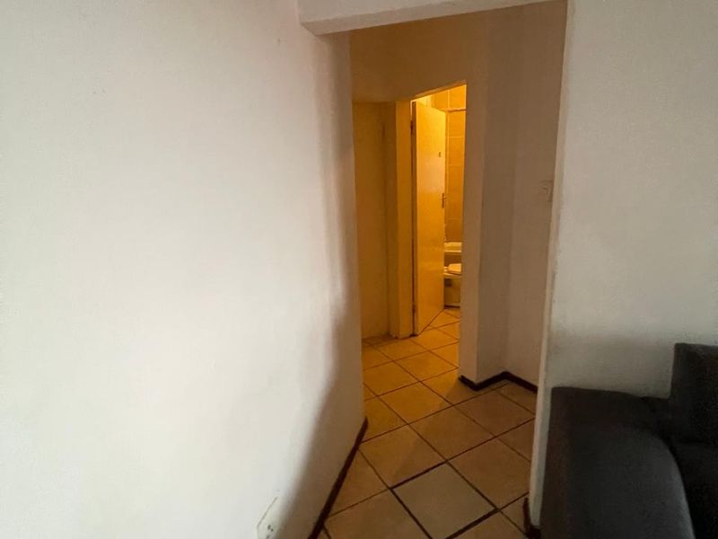 A narrow hallway with tiled flooring leading towards a bathroom area, featuring plain white walls and standard architectural finishes.