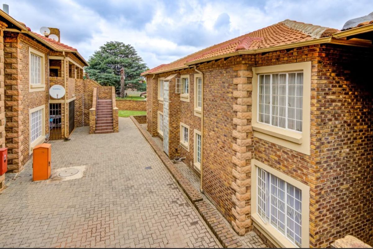 A view of the apartment complex exterior featuring face brick construction, terracotta tiled roofing, and a paved communal courtyard area with external stair access.