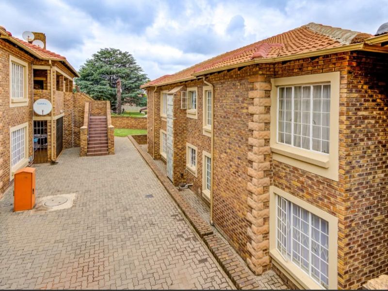 A view of the apartment complex exterior featuring face brick construction, terracotta tiled roofing, and a paved communal courtyard area with external stair access.