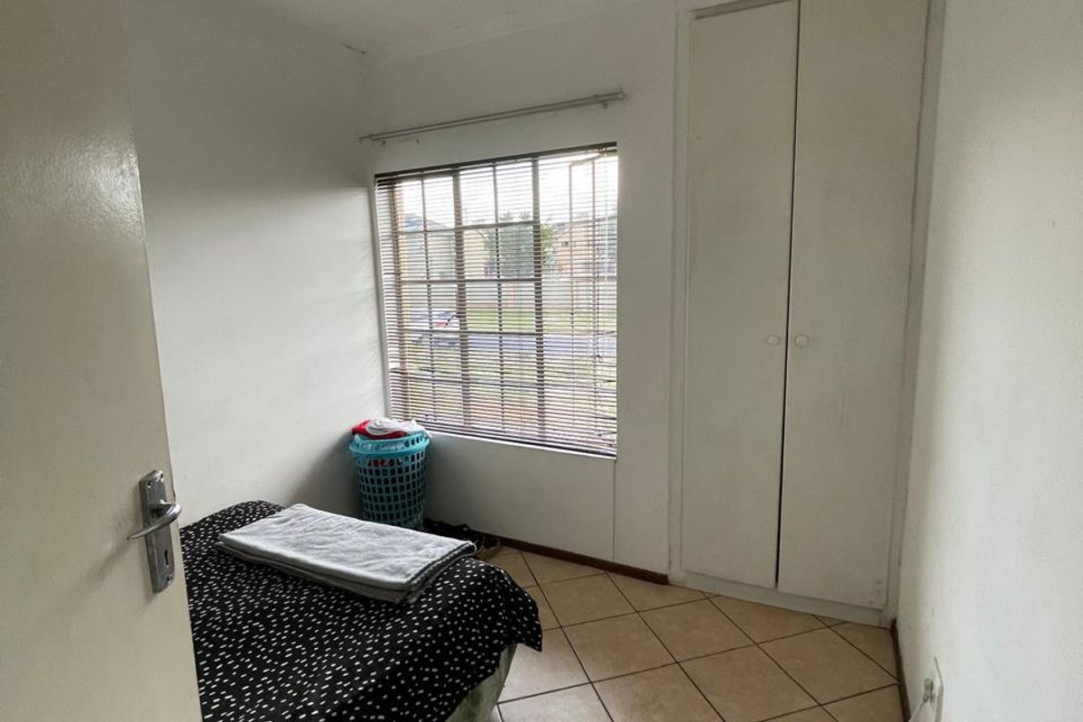 A compact bedroom featuring tiled flooring, a built-in wardrobe, and a window fitted with venetian blinds.